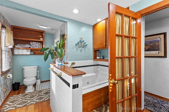 722 E 18th St, Ada, OK 74820 - full bath featuring wood finished floors, a jetted tub, toilet, a textured wall, and a textured ceiling
