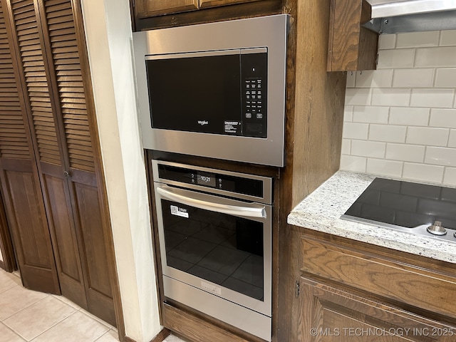 2806 E 84th St Unit 3, Tulsa, OK 74137 - kitchen with stainless steel appliances, light tile patterned flooring, exhaust hood, light stone counters, and decorative backsplash