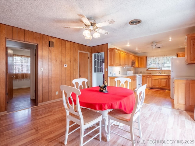 1412 S 9th, Mcalester, OK 74501 - dining space featuring a ceiling fan, healthy amount of natural light, light wood finished floors, wooden walls, and a textured ceiling