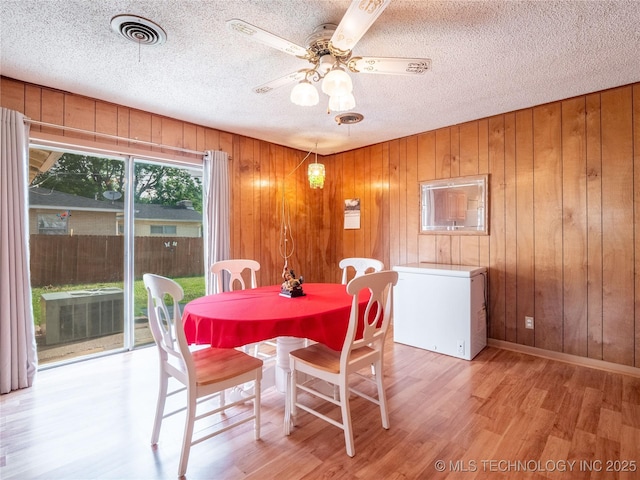 1412 S 9th, Mcalester, OK 74501 - dining room featuring light wood-style floors, a ceiling fan, a textured ceiling, and wooden walls