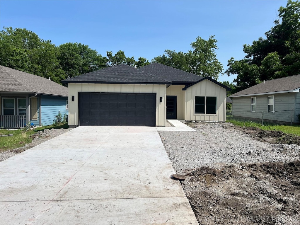 1907 E 27th St N, Tulsa, OK 74110 - view of front of home featuring board and batten siding, an attached garage, a shingled roof, and concrete driveway