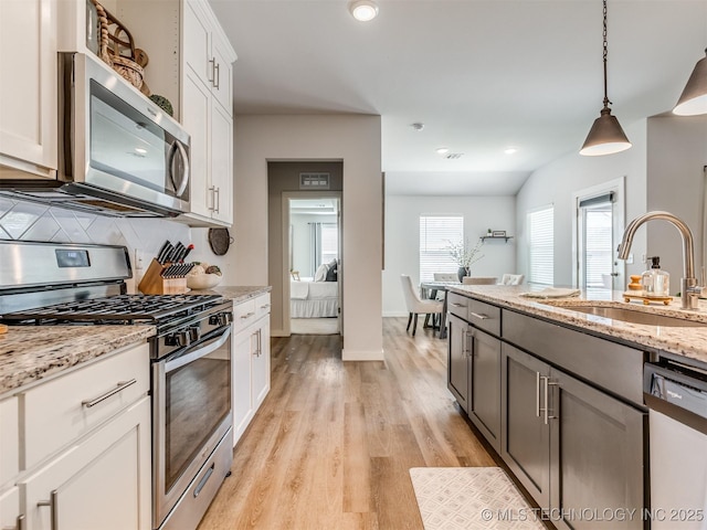 7221 S Indianwood Ave, Broken Arrow, OK 74011 - kitchen featuring appliances with stainless steel finishes, a sink, light wood finished floors, decorative backsplash, and light stone countertops