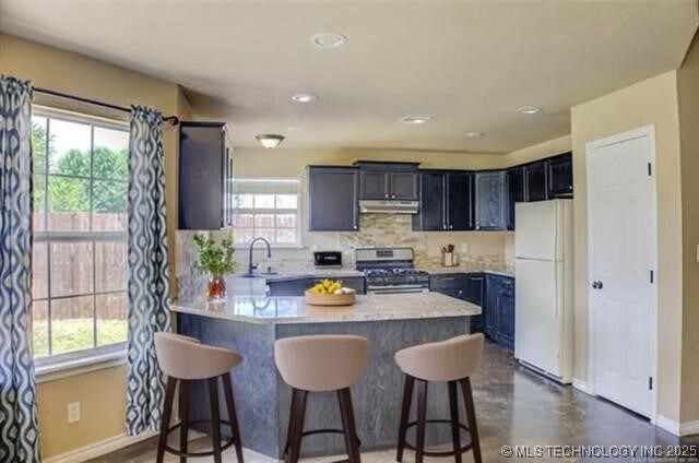 11968 S 270th E Ave, Coweta, OK 74429 - kitchen featuring stainless steel gas stove, freestanding refrigerator, under cabinet range hood, a peninsula, and a kitchen bar