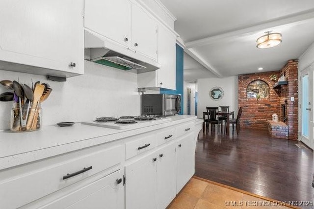 1138 N Gum Ave, Broken Arrow, OK 74012 - kitchen with stainless steel microwave, under cabinet range hood, light countertops, white cabinetry, and white cooktop