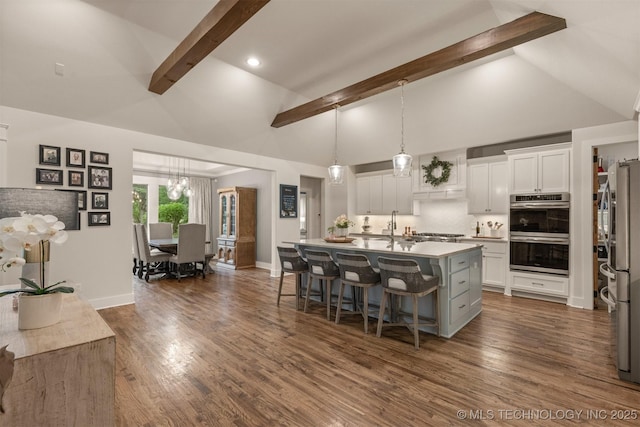6705 S Palm Ave, Broken Arrow, OK 74011 - kitchen with beam ceiling, appliances with stainless steel finishes, a breakfast bar, white cabinets, and an island with sink