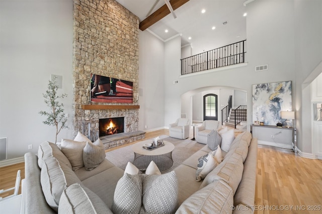 18319 E Red Fox Trl, Owasso, OK 74055 - living room featuring arched walkways, wood finished floors, a fireplace, beam ceiling, and a high ceiling