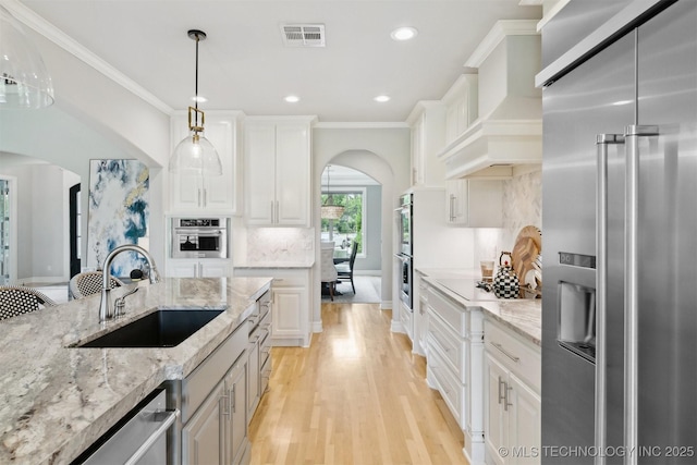 18319 E Red Fox Trl, Owasso, OK 74055 - kitchen with stainless steel appliances, arched walkways, a sink, light wood-type flooring, and light stone counters