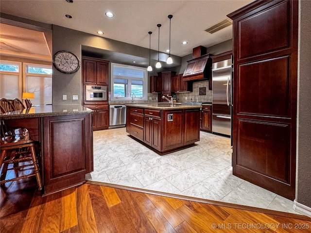 4418 N Little, Cushing, OK 74023 - kitchen featuring stainless steel appliances, decorative backsplash, an island with sink, custom range hood, and decorative light fixtures