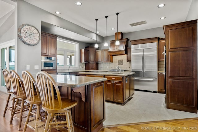4418 N Little, Cushing, OK 74023 - kitchen featuring appliances with stainless steel finishes, an island with sink, premium range hood, tasteful backsplash, and recessed lighting