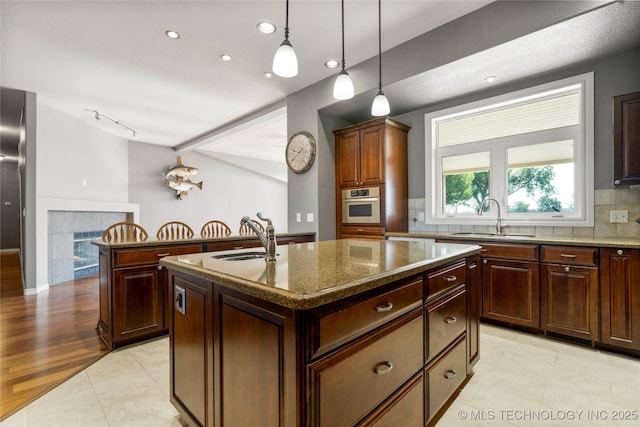 4418 N Little, Cushing, OK 74023 - kitchen featuring a center island with sink, decorative backsplash, stainless steel oven, dark stone counters, and decorative light fixtures