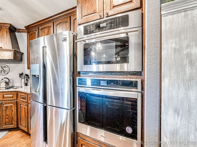 830294 S 3530, Stroud, OK 74079 - kitchen with stainless steel fridge, custom exhaust hood, brown cabinets, a textured ceiling, and light wood-type flooring