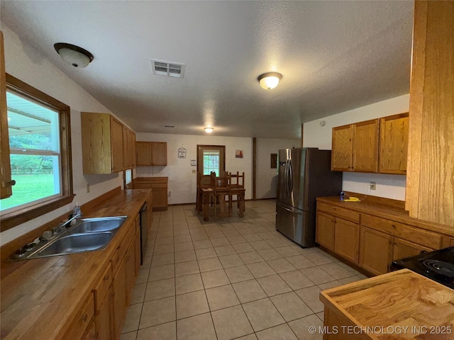 111 Hickory, Durant, OK 74731 - kitchen featuring freestanding refrigerator, light tile patterned floors, a sink, brown cabinetry, and butcher block counters