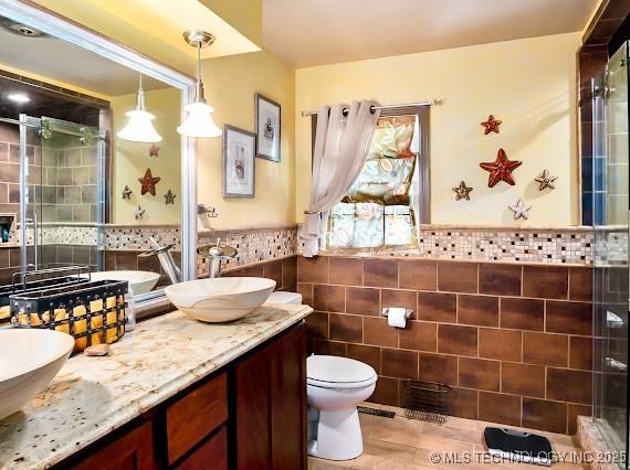 801 S Rennie St, Ada, OK 74820 - bathroom with tile walls, double vanity, a stall shower, and wainscoting