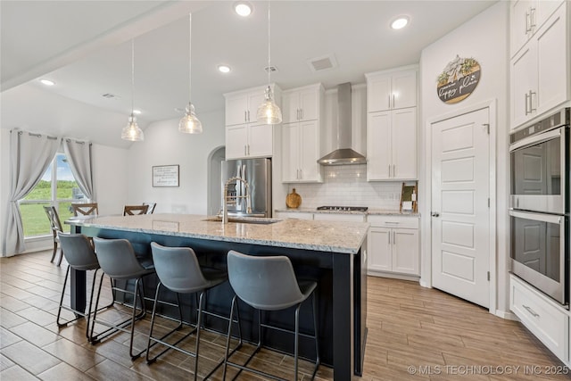 7000 S Elder Ave, Broken Arrow, OK 74011 - kitchen with wall chimney exhaust hood, appliances with stainless steel finishes, a breakfast bar area, light wood-style flooring, and an island with sink
