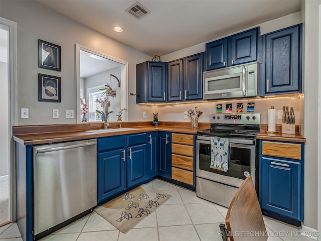 3215 W 41st St, Tulsa, OK 74107 - kitchen with stainless steel appliances, a sink, blue cabinets, light tile patterned floors, and recessed lighting