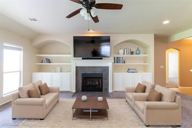 324 E 125th Pl S, Jenks, OK 74037 - living area with a ceiling fan, arched walkways, built in features, a tiled fireplace, and light colored carpet