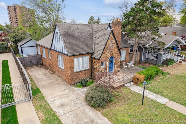 2124 E 19th St, Tulsa, OK 74104 - tudor house featuring a gate, a chimney, brick siding, a shingled roof, and concrete driveway
