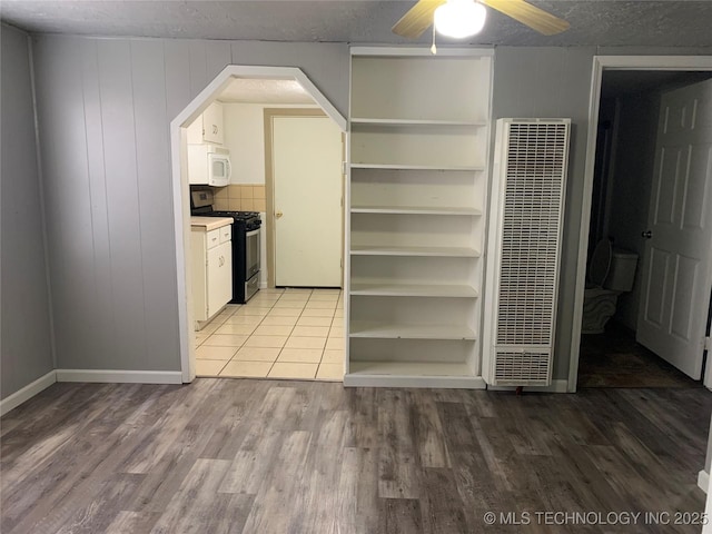 921 E 2nd St, Cushing, OK 74023 - kitchen with gas range, white microwave, a heating unit, wood finished floors, and a ceiling fan