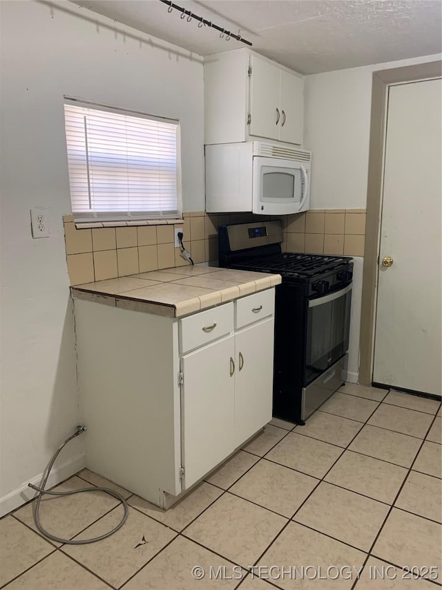 921 E 2nd St, Cushing, OK 74023 - kitchen featuring gas range, white microwave, backsplash, tile counters, and light tile patterned floors
