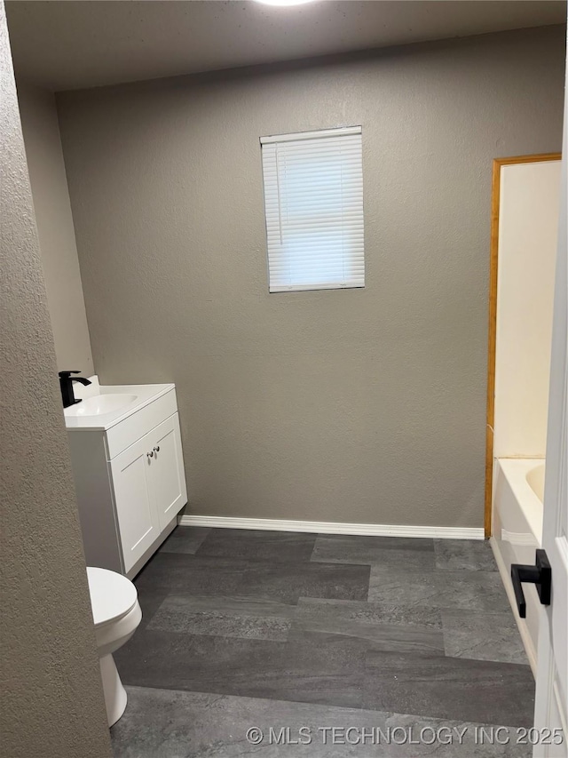 910 E Maple St, Cushing, OK 74023 - bathroom featuring toilet, vanity, wood finished floors, a bath, and baseboards