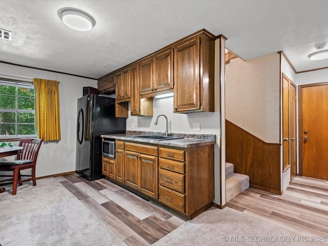 1800 SE Polaris Dr, Bartlesville, OK 74006 - kitchen featuring stainless steel microwave, freestanding refrigerator, light wood-style floors, a textured ceiling, and brown cabinets