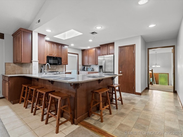1800 SE Polaris Dr, Bartlesville, OK 74006 - kitchen featuring black microwave, a peninsula, stainless steel fridge with ice dispenser, backsplash, and light stone counters