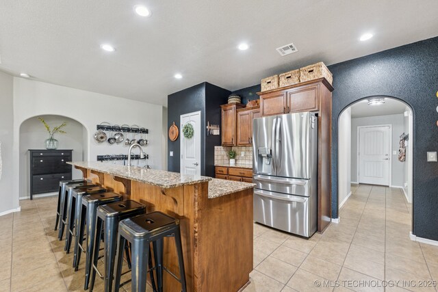 14201 E 101st St, Owasso, OK 74055 - kitchen with stainless steel fridge with ice dispenser, arched walkways, light stone countertops, light tile patterned floors, and a center island with sink