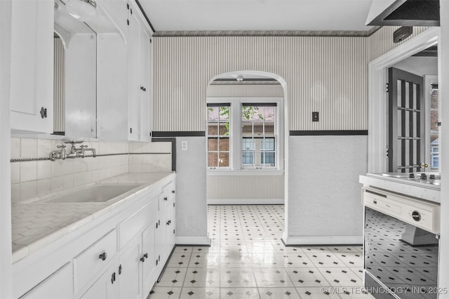 2728 E 13th Pl, Tulsa, OK 74104 - kitchen featuring wallpapered walls, white cabinets, a sink, light floors, and baseboards