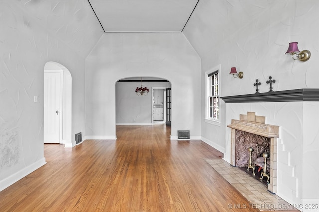 2728 E 13th Pl, Tulsa, OK 74104 - unfurnished living room featuring arched walkways, vaulted ceiling, wood finished floors, and a chandelier