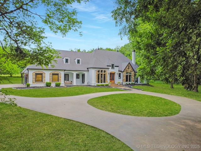 9914 S Garnett Rd, Broken Arrow, OK 74012 - french country style house featuring curved driveway, a chimney, stone siding, and a front yard
