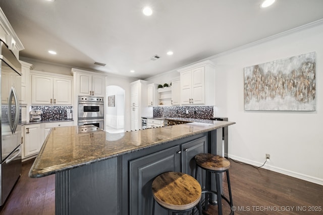 9914 S Garnett Rd, Broken Arrow, OK 74012 - kitchen with open shelves, white cabinetry, a breakfast bar, stainless steel appliances, and backsplash