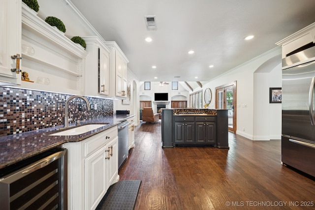 9914 S Garnett Rd, Broken Arrow, OK 74012 - kitchen with wine cooler, a sink, appliances with stainless steel finishes, arched walkways, and a lit fireplace