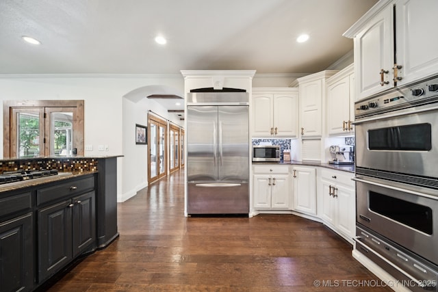 9914 S Garnett Rd, Broken Arrow, OK 74012 - kitchen with appliances with stainless steel finishes, arched walkways, white cabinets, tasteful backsplash, and ornamental molding
