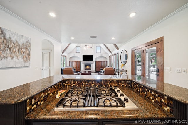 9914 S Garnett Rd, Broken Arrow, OK 74012 - kitchen featuring stainless steel gas stovetop, a ceiling fan, a warm lit fireplace, dark stone counters, and recessed lighting