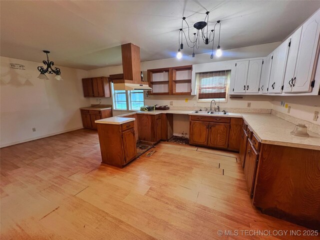 5006 S 449th Ave W, Jennings, OK 74038 - kitchen featuring a sink, a peninsula, a chandelier, light wood finished floors, and brown cabinets