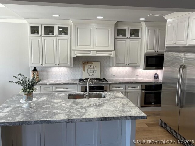 3816 E 117th Pl, Tulsa, OK 74137 - kitchen featuring appliances with stainless steel finishes, a sink, white cabinetry, glass insert cabinets, and light stone counters
