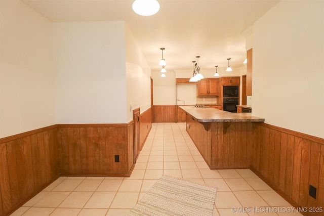 9337 S Lakewood Ave, Tulsa, OK 74137 - kitchen with wainscoting, black appliances, wood walls, brown cabinetry, and light tile patterned floors