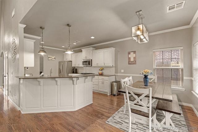 5006 S 164th E Ave, Tulsa, OK 74134 - kitchen with appliances with stainless steel finishes, wood finished floors, tasteful backsplash, white cabinetry, and ornamental molding