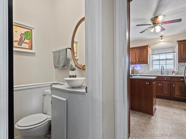 1629 Dewey Ave, Bartlesville, OK 74003 - bathroom with vanity, toilet, wainscoting, ceiling fan, and decorative backsplash