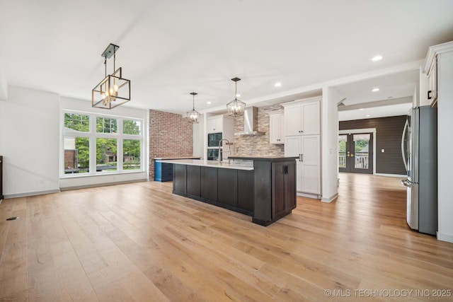 1611 S Lewis Pl, Tulsa, OK 74104 - kitchen with freestanding refrigerator, wall chimney range hood, a chandelier, white cabinets, and light wood-style floors