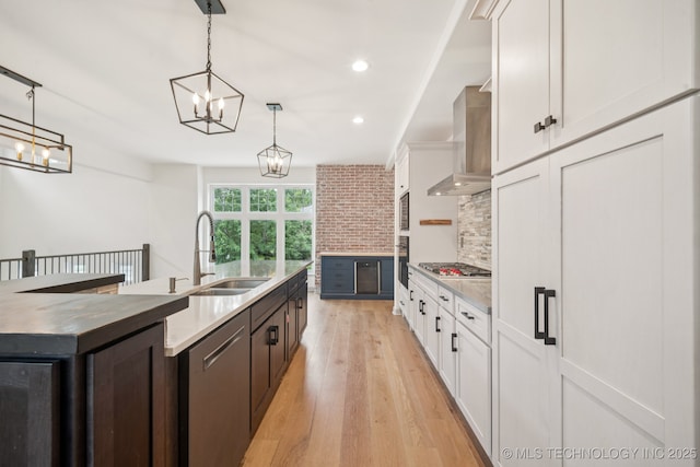 1611 S Lewis Pl, Tulsa, OK 74104 - kitchen featuring wall chimney range hood, white cabinetry, appliances with stainless steel finishes, light wood-style floors, and pendant lighting