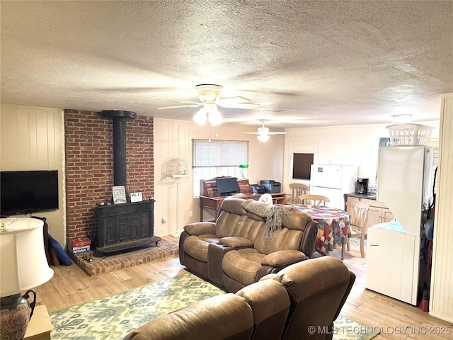 421224 E 1165th Rd, Eufaula, OK 74432 - living area featuring a wood stove, light wood-style flooring, a ceiling fan, a textured ceiling, and wood walls