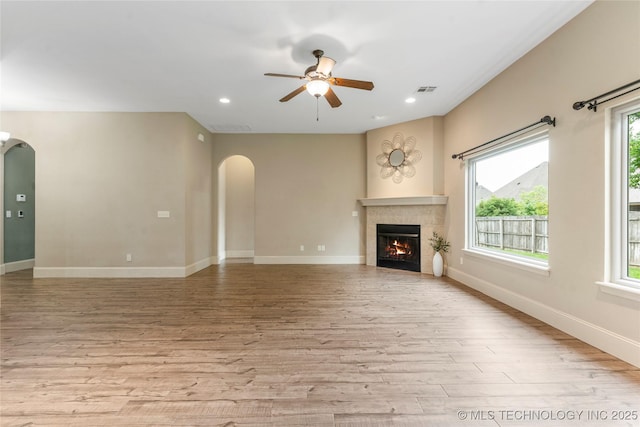 4675 E 144th Pl S, Bixby, OK 74008 - unfurnished living room featuring arched walkways, ceiling fan, light wood finished floors, a tile fireplace, and baseboards