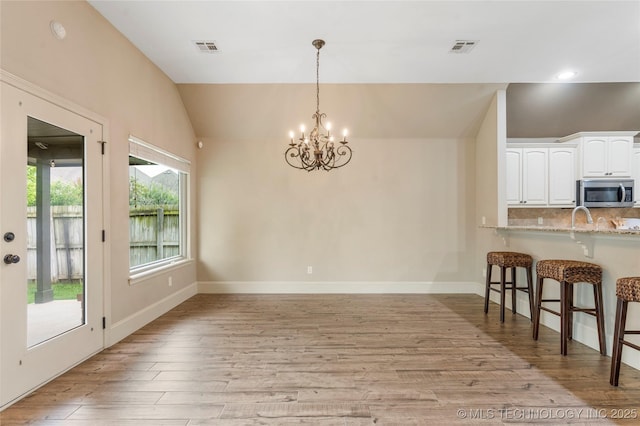 4675 E 144th Pl S, Bixby, OK 74008 - kitchen with stainless steel microwave, a kitchen bar, a chandelier, lofted ceiling, and light wood finished floors