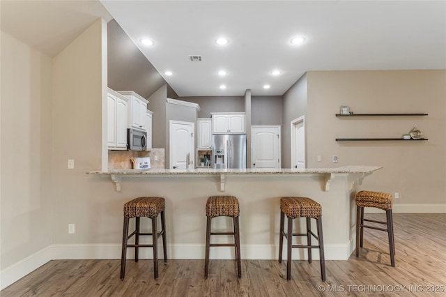 4675 E 144th Pl S, Bixby, OK 74008 - kitchen featuring stainless steel appliances, a kitchen bar, a peninsula, white cabinets, and light wood-style floors