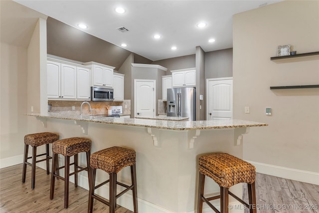 4675 E 144th Pl S, Bixby, OK 74008 - kitchen with appliances with stainless steel finishes, a peninsula, light wood finished floors, a kitchen bar, and baseboards