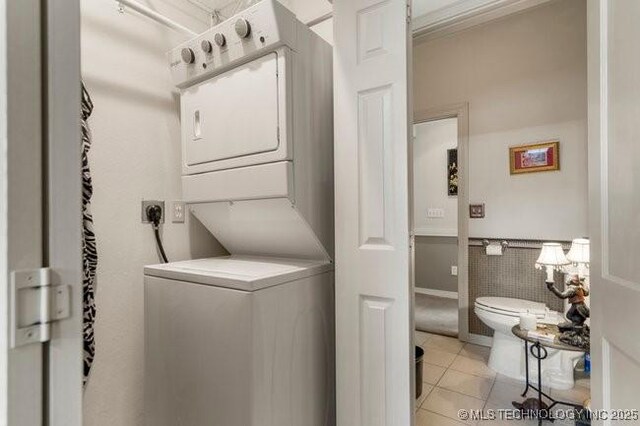 2403 S Troost Ave, Tulsa, OK 74114 - laundry room with stacked washer and clothes dryer, light tile patterned floors, wainscoting, and tile walls