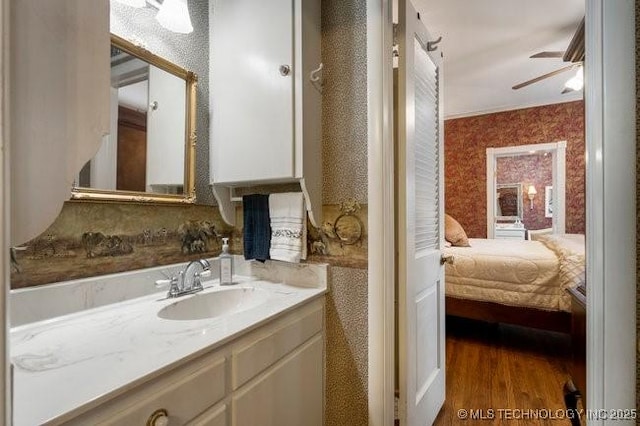 2403 S Troost Ave, Tulsa, OK 74114 - ensuite bathroom featuring wallpapered walls, vanity, a ceiling fan, and wood finished floors