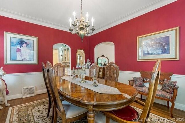 2403 S Troost Ave, Tulsa, OK 74114 - dining room featuring arched walkways, a chandelier, wood finished floors, and ornamental molding