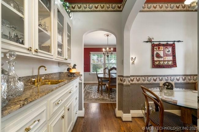 2403 S Troost Ave, Tulsa, OK 74114 - indoor wet bar featuring arched walkways, dark wood-type flooring, crown molding, a chandelier, and baseboards